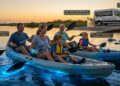 A happy family using bioluminescent kayaking paddles to stir up glowing water at Merritt Island National Wildlife Refuge, illustrating the best eco-tours for families in Orlando.
