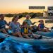 A happy family using bioluminescent kayaking paddles to stir up glowing water at Merritt Island National Wildlife Refuge, illustrating the best eco-tours for families in Orlando.